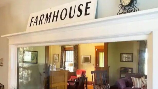 A view through a window labeled 'FARMHOUSE' into a living room with a fireplace, a sofa, and a coffee table. - Entire farmhouse in the country (Winterset)