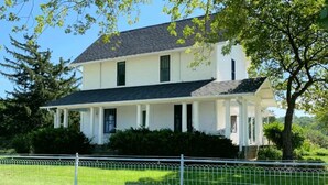 A two-story white house with a porch, surrounded by a white fence and greenery. - Entire farmhouse in the country (Winterset)