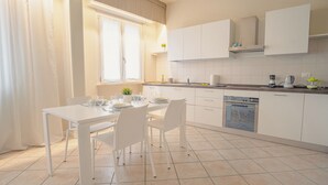 A modern kitchen with white cabinetry, a dining table set for four, and a built-in dishwasher. - Sweet Lake Apartment (Sirmione)
