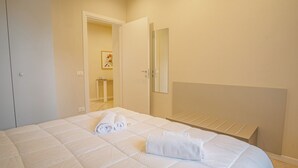 A bedroom with a bed, a mirror, and a door leading to a bathroom. - Sweet Lake Apartment (Sirmione)