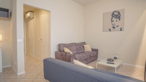 A living room with a sofa, a coffee table, a TV, and a door leading to a hallway. - Sweet Lake Apartment (Sirmione)