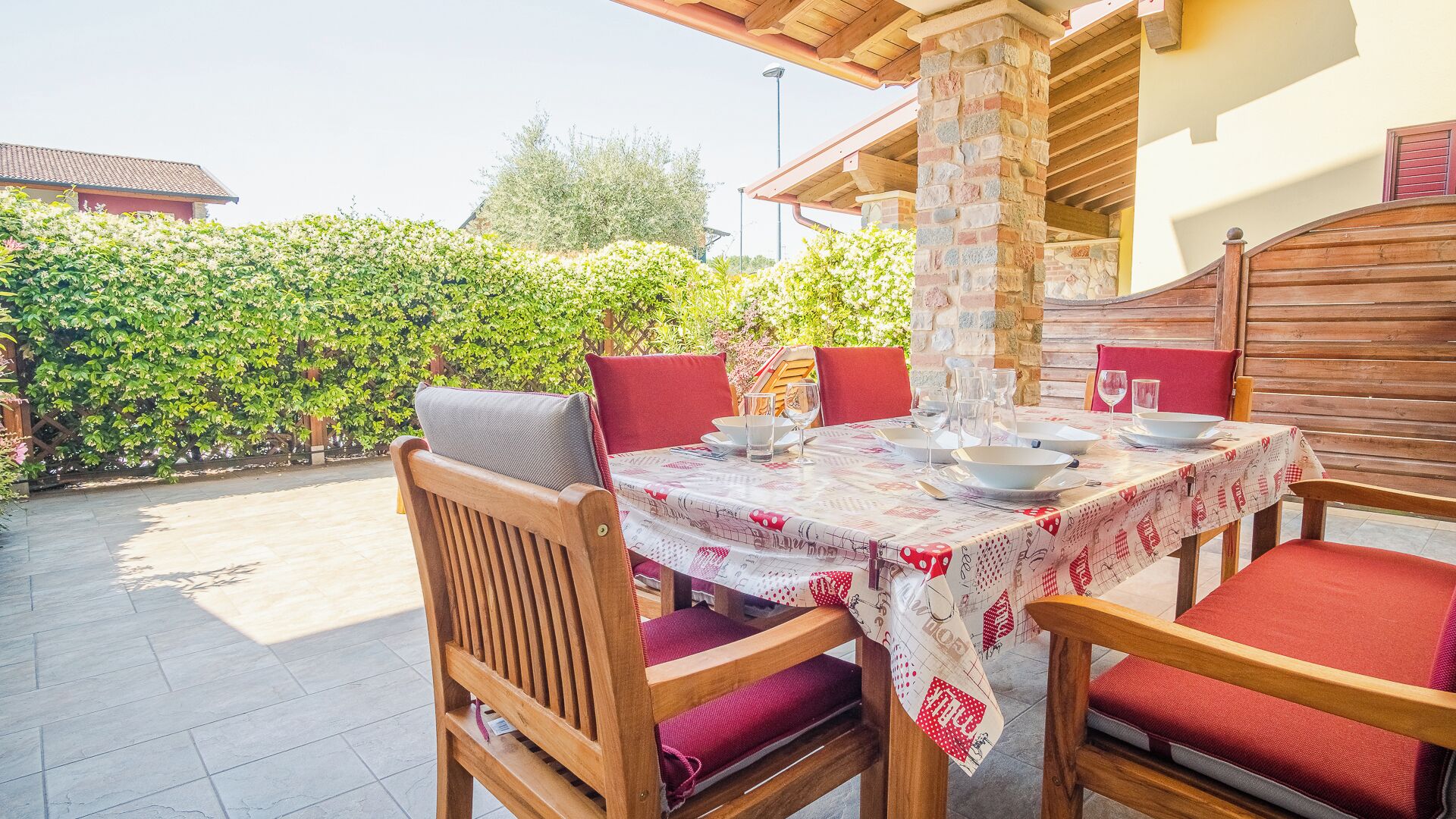Un espace de restauration en plein air avec une table dressée pour quatre personnes, entourée de chaises en bois dotées de coussins rouges.