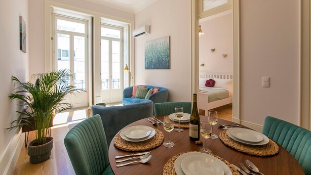 Un comedor con una mesa de madera preparada para cuatro personas, rodeada de sillas tapizadas en verde.