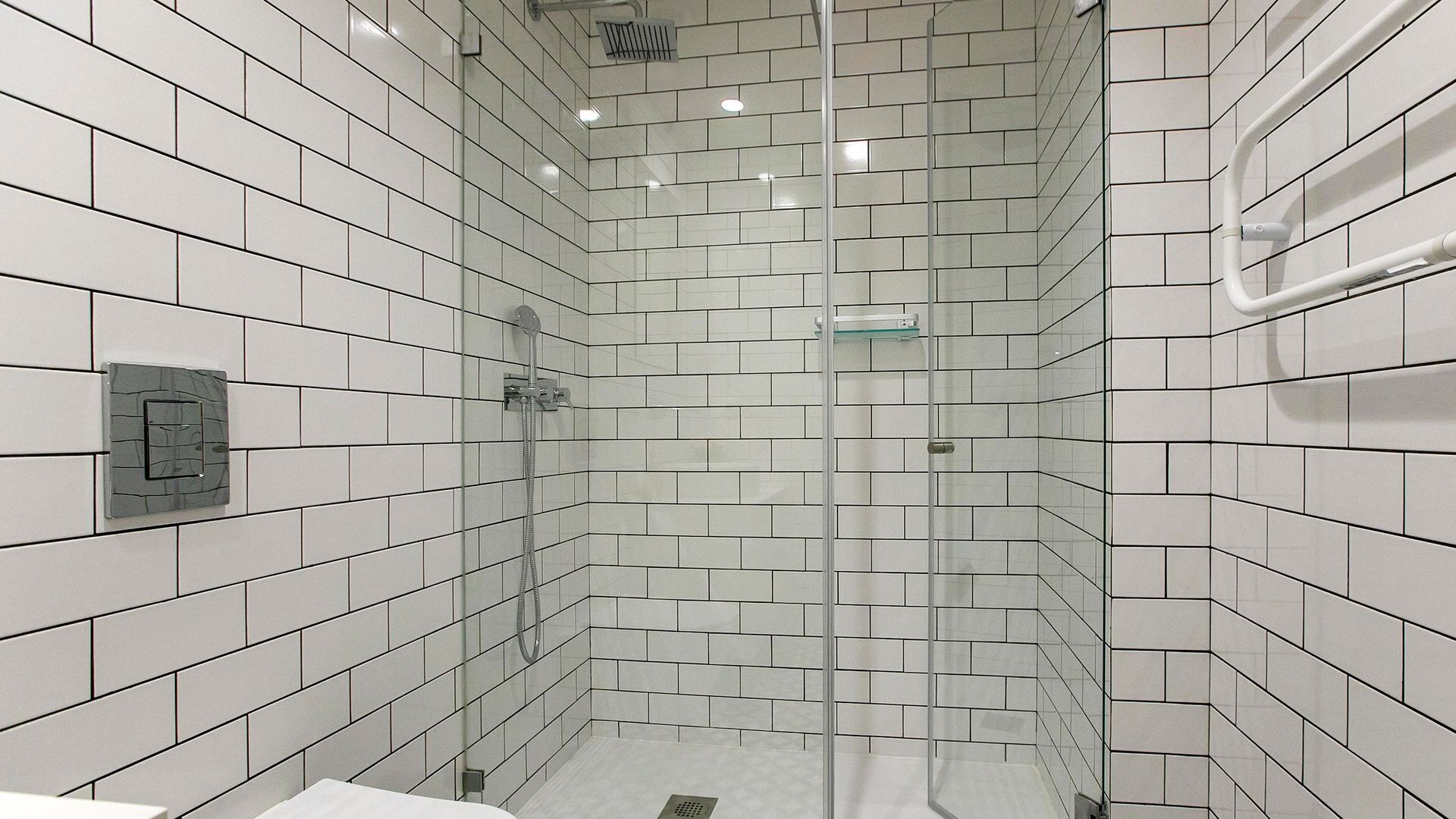 A modern bathroom with white subway tiles, a glass shower enclosure, and a visible control panel.