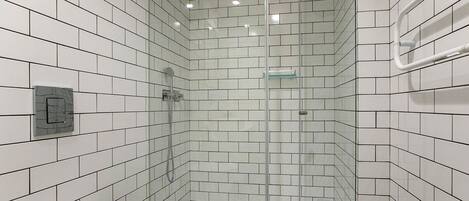 A modern bathroom with white subway tiles, a glass shower enclosure, and a visible control panel.