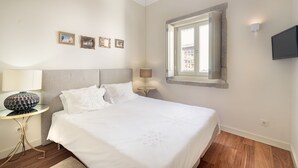 A bedroom with a bed, a bedside table with a lamp, a small round table, and a wall-mounted TV. - Gold Oporto Home River Front - Ribeira (Vila Nova de Gaia)