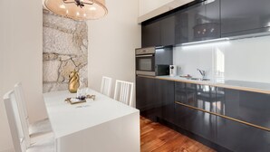 A modern kitchen with dark cabinets, a white countertop, and a stone wall. - Gold Oporto Home River Front - Ribeira (Vila Nova de Gaia)
