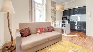 A modern living room with a sofa, a dining table, and chairs. There is a kitchen area with a stove and cabinets. - Gold Oporto Home River Front - Ribeira (Vila Nova de Gaia)