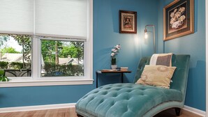A room with a teal upholstered chair, a small side table with a plant, and a window with blinds. - Spacious Midcentury home located 1 block from Oaklawn Racing and Gaming (Hot Springs)