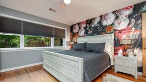 A bedroom with a large bed, a nightstand, a wall mural, and a window with blinds. - Spacious Midcentury home located 1 block from Oaklawn Racing and Gaming (Hot Springs)