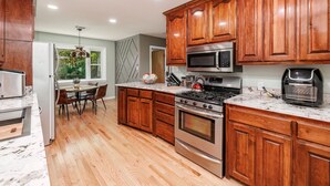 A modern kitchen with wooden cabinets, stainless steel appliances, and a dining area with a table and chairs. - Spacious Midcentury home located 1 block from Oaklawn Racing and Gaming (Hot Springs)