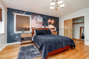 A bedroom with a large bed, a wooden headboard, a nightstand, a lamp, a fluffy rug, and a wall mural.