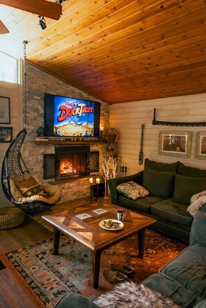 A cozy living room with a fireplace, a television displaying 'Disney DuckTales', and comfortable seating.
