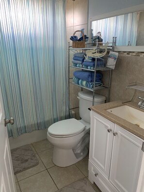 Bathroom features a toilet, sink, and storage shelf with towels and a basket.