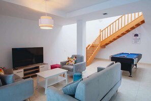 A living room with a flat-screen TV, a pool table, a staircase, and a sofa.