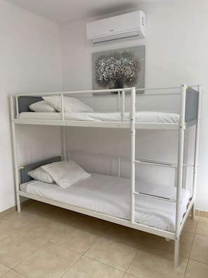 A bunk bed with a white frame and bedding, an air conditioning unit above, and a decorative wall piece.