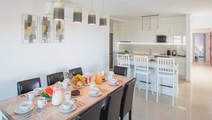 Een moderne eetruimte met een houten tafel gedekt voor ontbijt, witte stoelen en hanglampen.