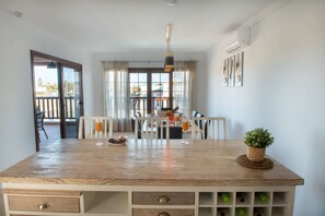 A kitchen with a wooden island, a dining table with chairs, a hanging pendant light, and a view through the window.