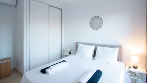 Een hotelkamer met een bed, een nachtkastje met een lamp, een wandklok en een kledingkast.