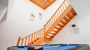 Een pooltafel met een houten trap en een dakraam erboven.