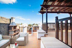 An outdoor patio area with wicker furniture, a barbecue grill, and a view of the surrounding landscape. - Villa Vista Rey - 6 Bedroom - Heated Pool - Amazing Views - Pool Table - Vista Lobos - Playa Blanca (Lanzarote)
