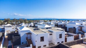 A coastal residential area with white buildings, some with flat roofs and others with sloped roofs, and a clear view of the sea and distant mountains. - Villa Vista Rey - 6 Bedroom - Heated Pool - Amazing Views - Pool Table - Vista Lobos - Playa Blanca (Lanzarote)