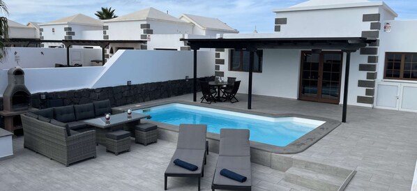 A poolside area with a built-in barbecue, seating, and a pergola.