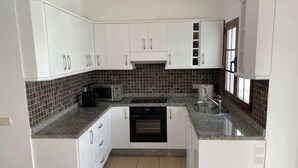 Cocina compacta con armarios blancos, microondas, cafetera y lavavajillas.