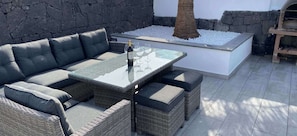 A wicker outdoor seating area with a glass-top table, cushioned chairs, and a stone wall backdrop.