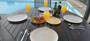 Una mesa dispuesta para dos personas, con platos, cubiertos, un vaso de zumo de naranja, una botella de aceite de oliva y una botella de vinagre balsámico.