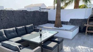 Un patio exterior con un sofá seccional, una mesa de vidrio y una pared de piedra.