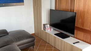 Una sala moderna con un televisor de pantalla plana grande sobre un mueble de madera, una lámpara colgante tejida, un sofá seccional gris grande y un cuadro en la pared.