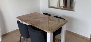 A dining table with a marble top and four chairs, positioned in a room with white walls and a tiled floor.