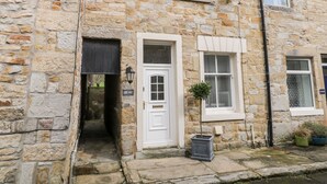 A stone building with a white door, a small window with shutters, and a potted plant in front. - Ermysted's Cottage (Skipton)