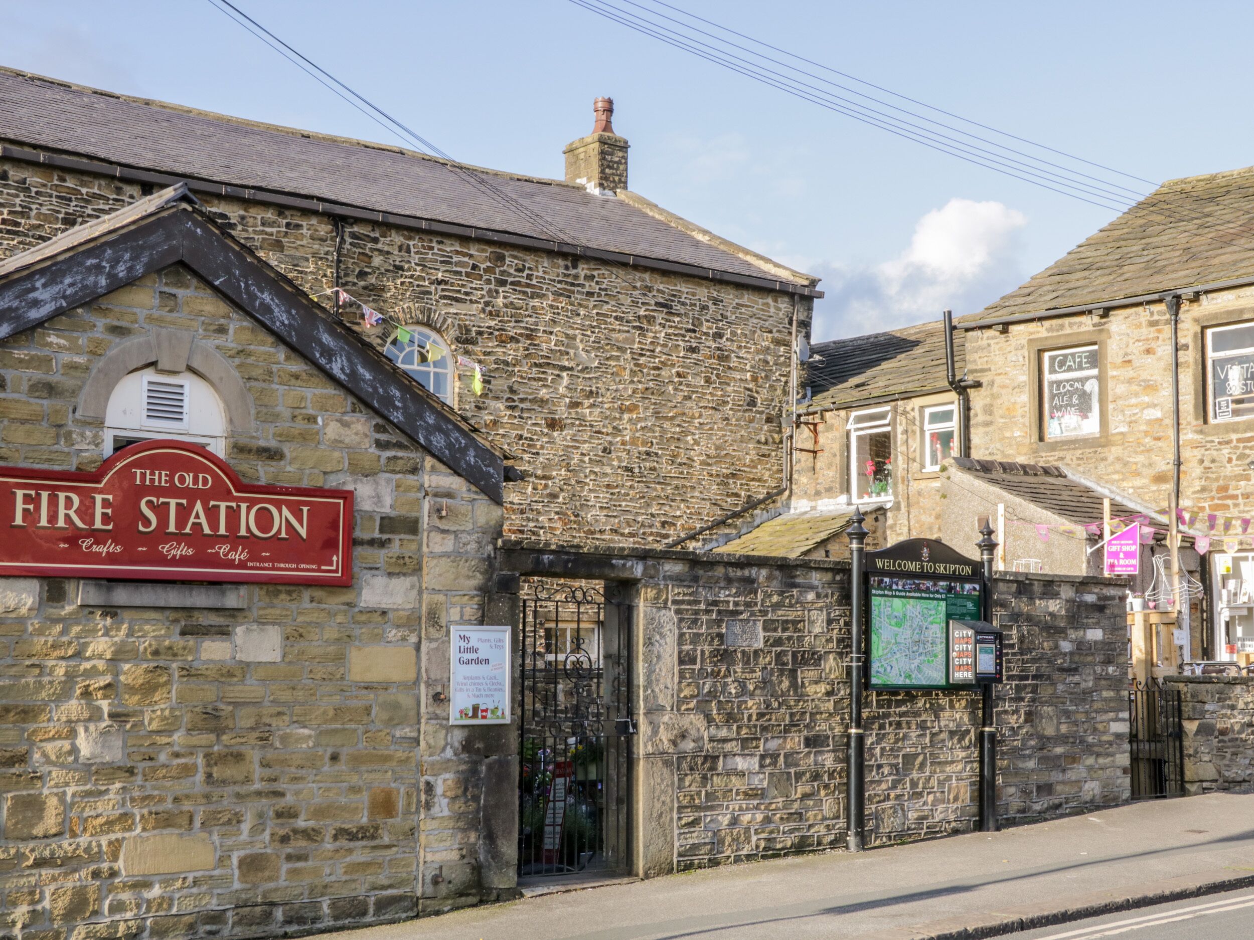 Een stenen gebouw met een bord waarop 'The Old Fire Station' staat en een ander bord met 'Welkom in Skipton'.