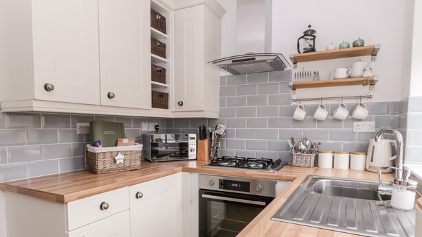 A modern kitchen with white cabinets, a wooden countertop, a built-in oven, a gas stove, and a stainless steel sink. - Ermysted's Cottage (Skipton)