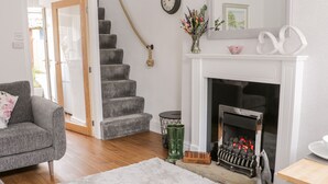 A living room with a fireplace, grey carpet, and a staircase. - Ermysted's Cottage (Skipton)