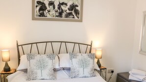 Una cama bien tendida con ropa blanca y dos almohadas con motivos de árboles, flanqueada por dos lámparas de noche.