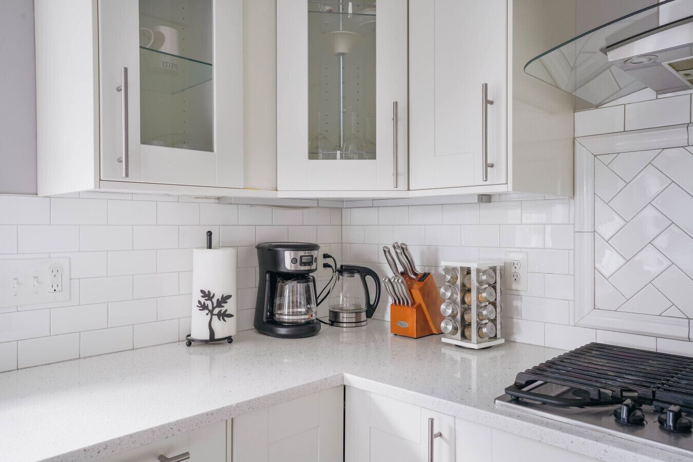 A modern kitchen with white cabinets, a coffee maker, a kettle, and a spice rack.