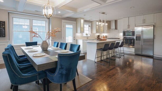 Una cocina amplia con electrodomésticos modernos, un comedor con sillas tapizadas en azul, y una isla grande con taburetes de bar.