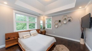 Un dormitorio con una cama grande, varias ventanas, cabecero de madera, alfombra mullida y decoración de pared hexagonal.