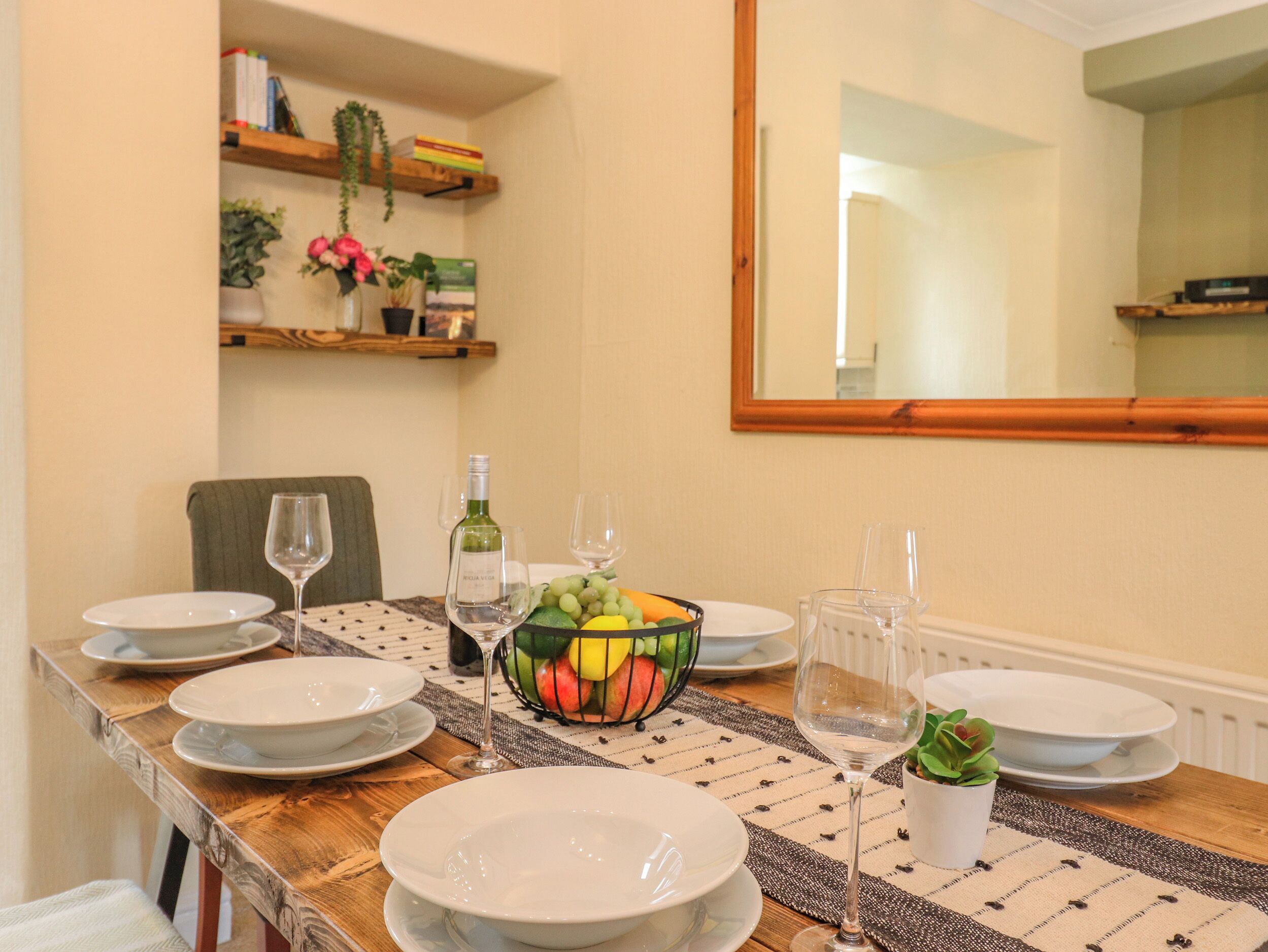 Una mesa de comedor dispuesta con platos, copas de vino y una cesta de frutas.