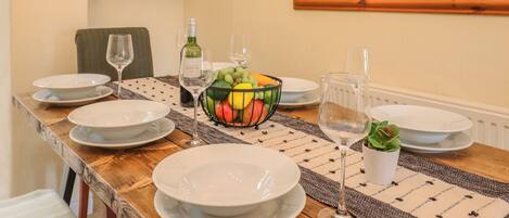 Una mesa de comedor dispuesta con platos, copas de vino y una cesta de frutas.