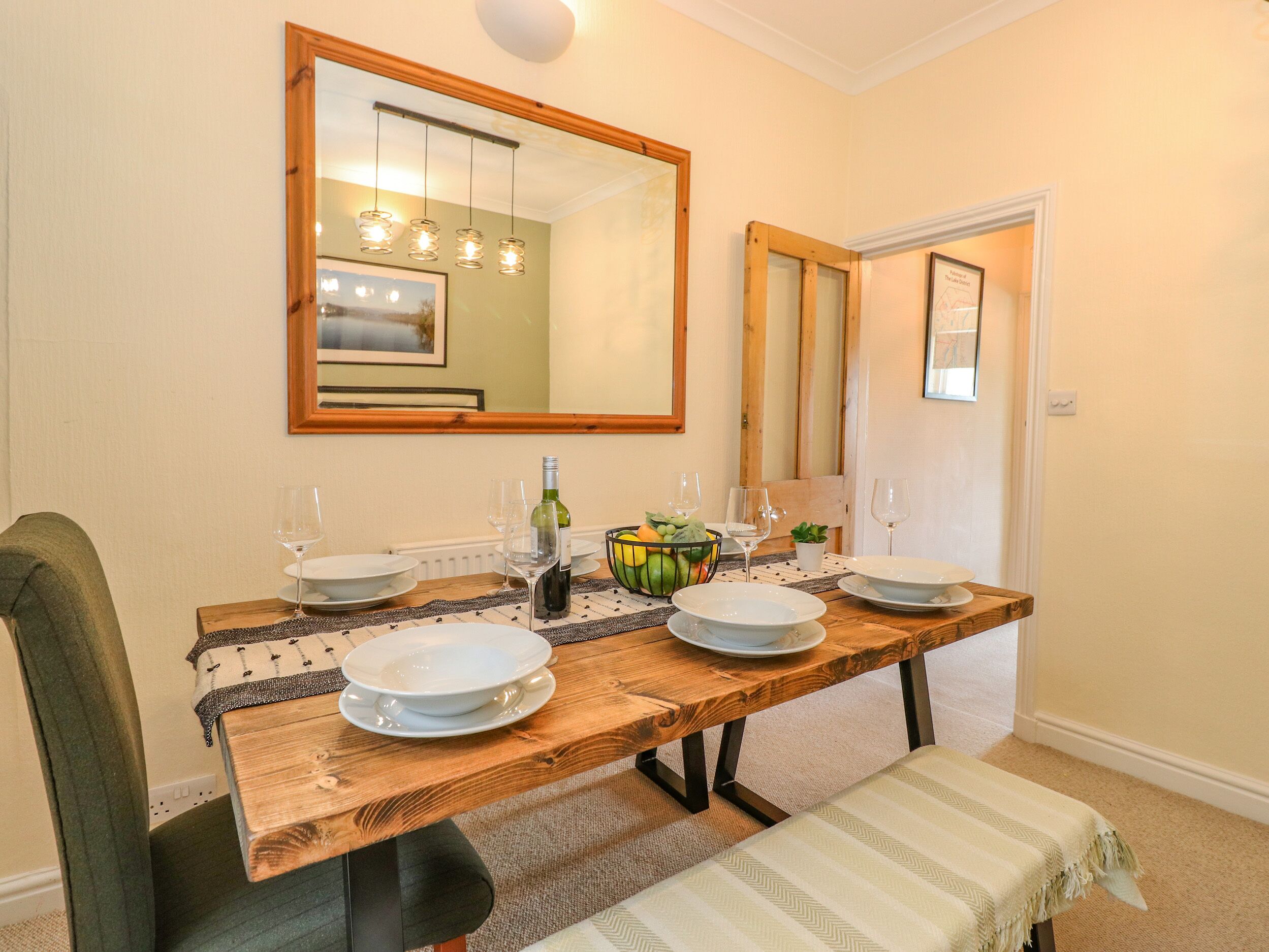 A dining room with a wooden table set for four, a large mirror above, and a door with a framed picture.