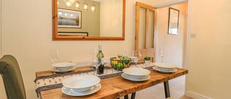 A dining room with a wooden table set for four, a large mirror above, and a door with a framed picture.
