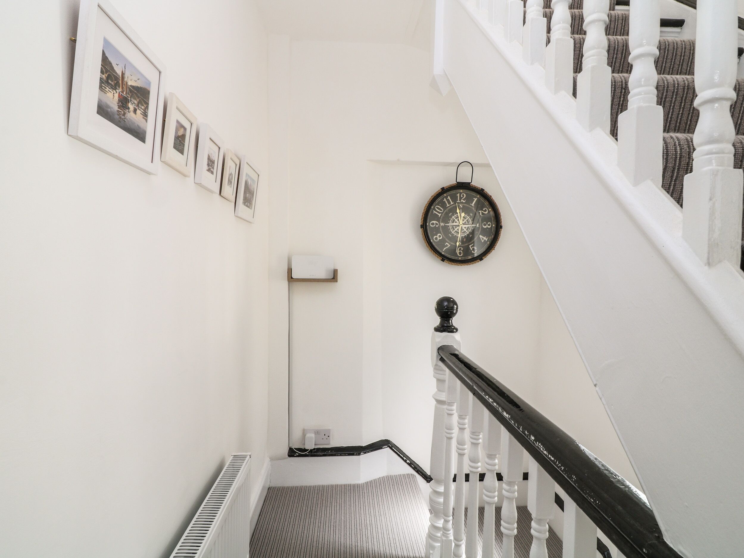 A staircase with white balusters and a black handrail, a wall-mounted clock, and framed pictures.