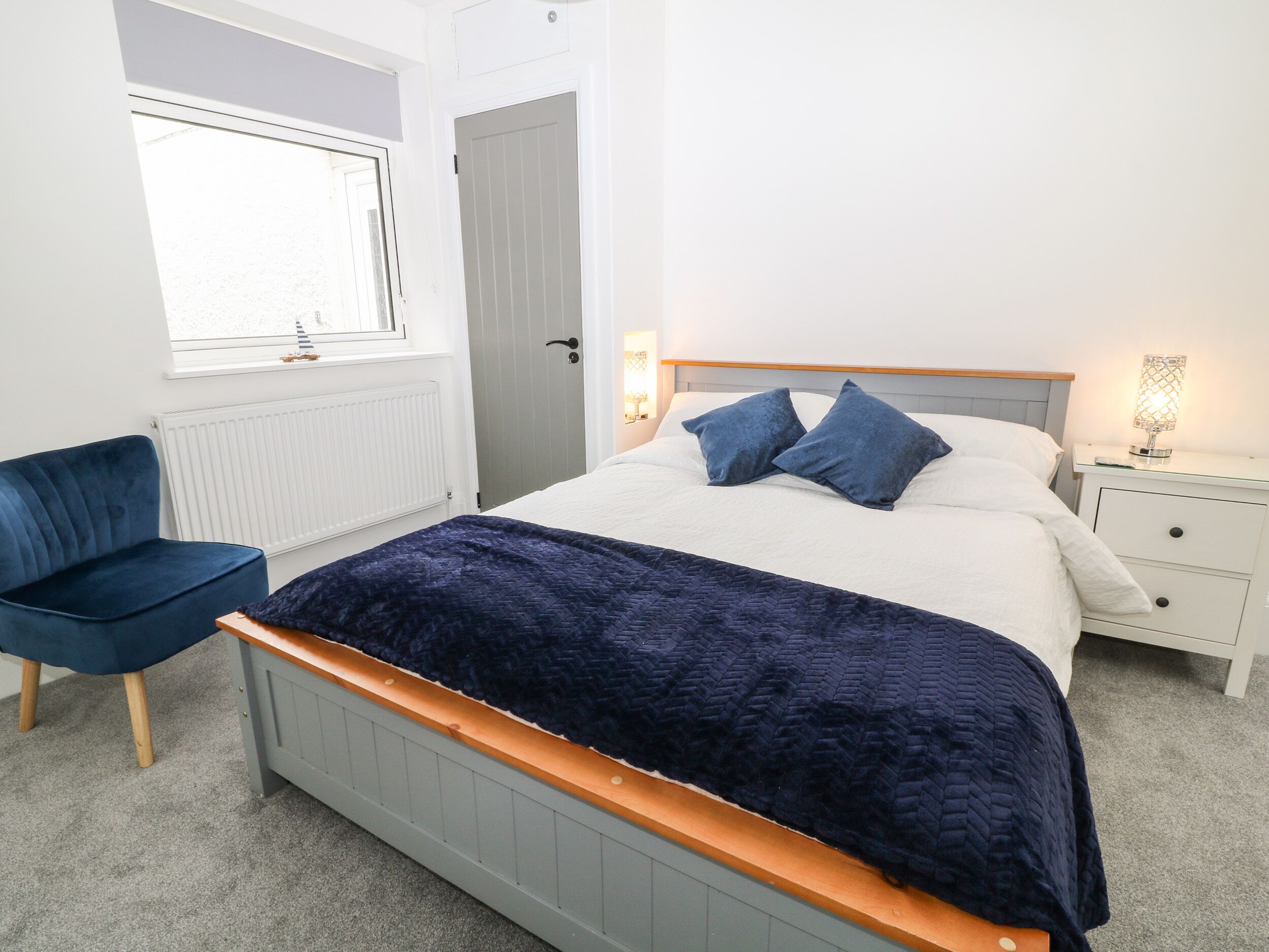 A bedroom with a bed, bedside table, lamp, and a chair.