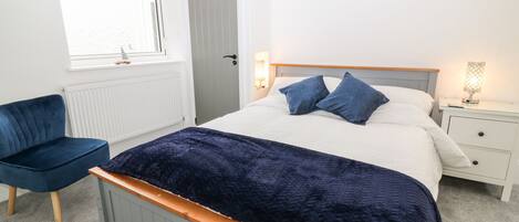 Un dormitorio con cama, mesita de noche, lámpara y una silla.