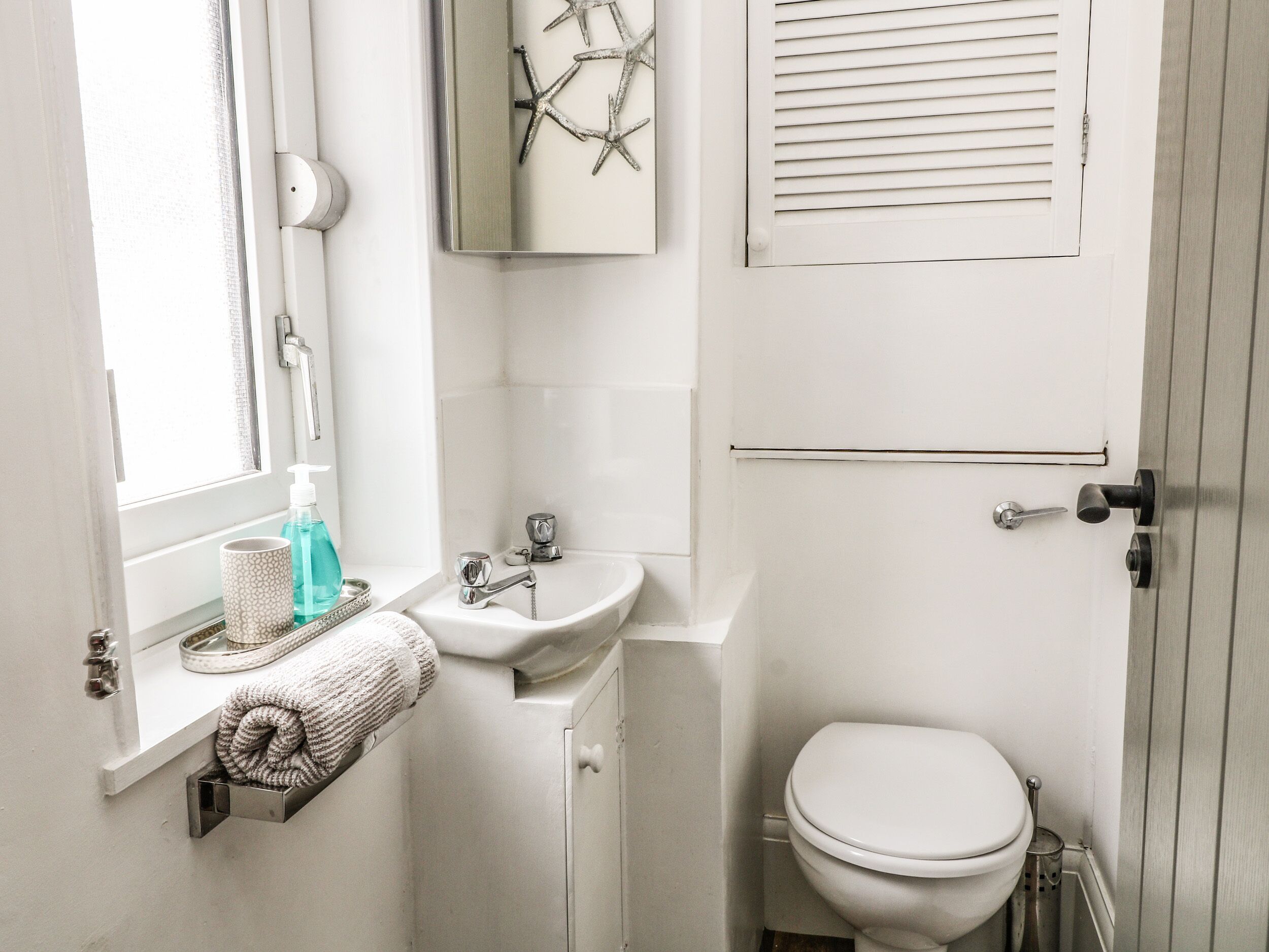 Un baño pequeño con lavamanos blanco, inodoro y ventana con persianas.