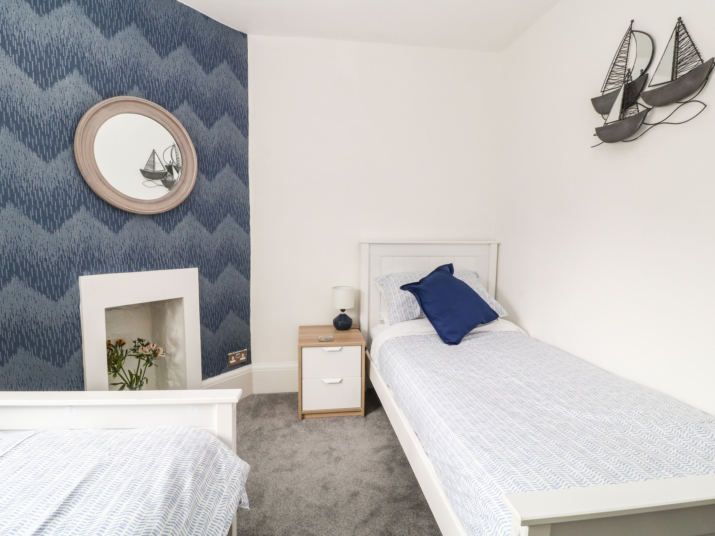 A bedroom with two beds, a nightstand, a mirror, and a wall-mounted ship decoration.